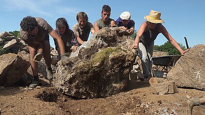 Six personnes unissent leurs forces en poussant un gros rocher dans le but de construire une fromagerie en estive